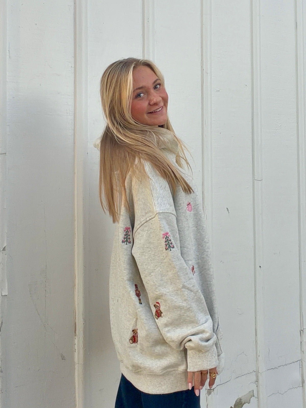Oatmeal Christmas hoodie shown from the side, with embroidered holiday motifs on the sleeves