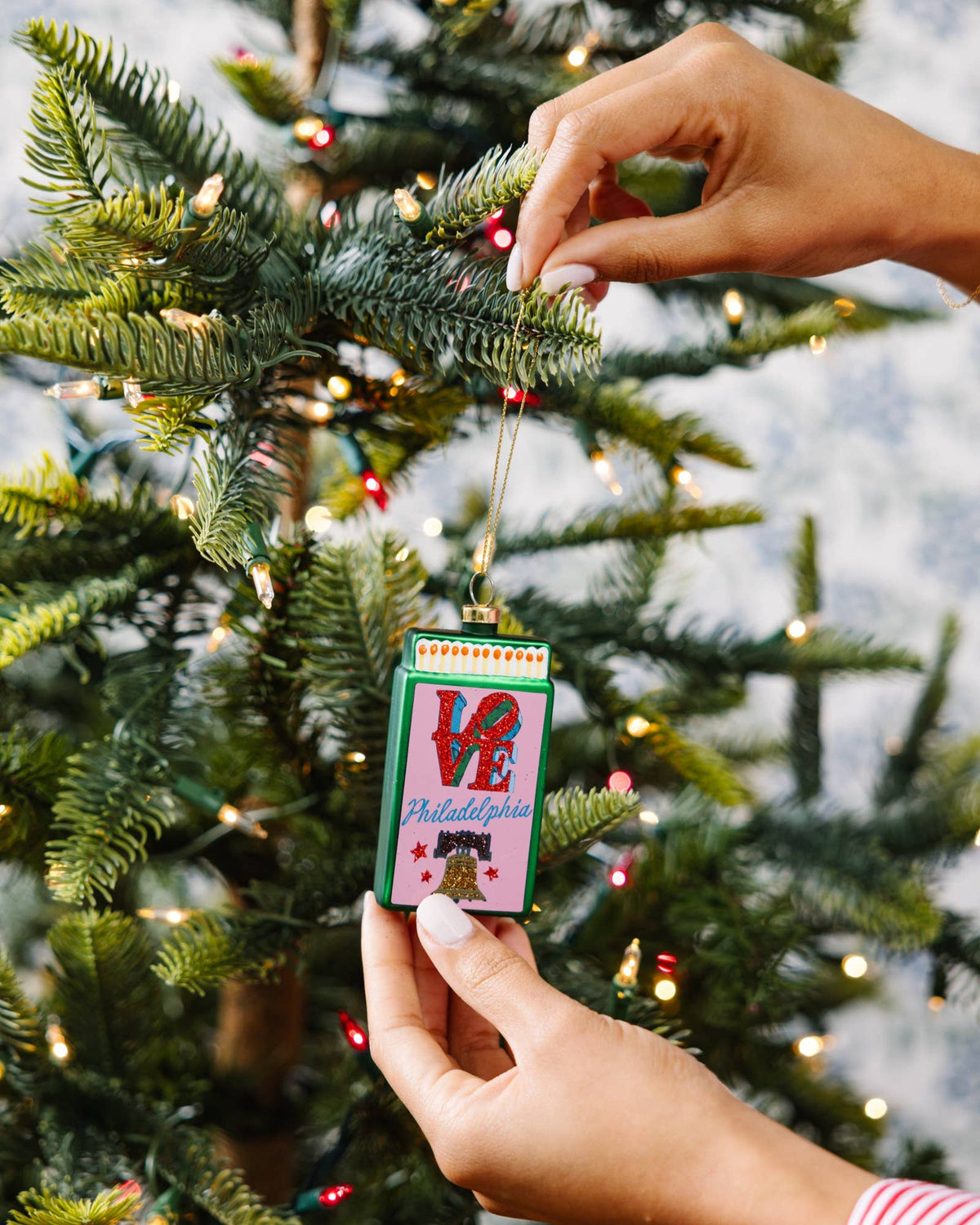 Matchbook ornament held near tree branches, green frame with LOVE and Philadelphia print.