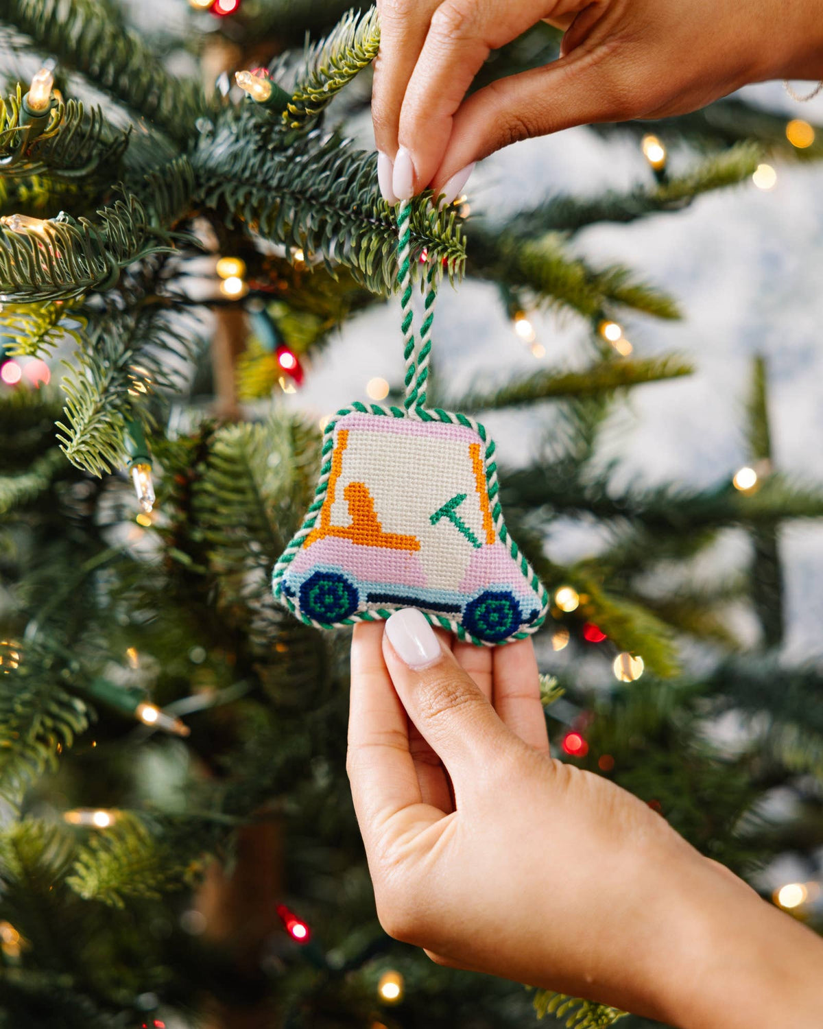 Needlepoint golf cart ornament with orange cart and blue wheels, green rope loop